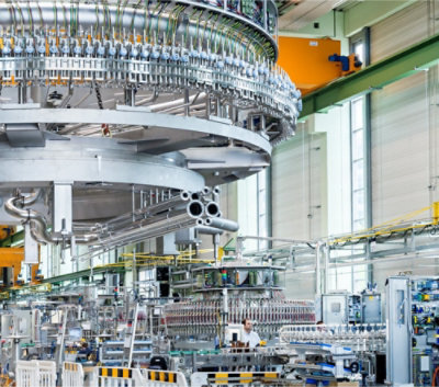 Industrieel interieur met complexe machines, leidingen en een medewerker in beschermende kleding. 