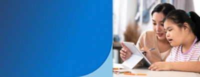 Two individuals focused on a tablet, with pencils and paper on the table, suggesting a learning or collaborative activity.