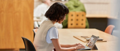 Persona che digita su un portatile a un tavolo di legno in uno spazio di lavoro interno.